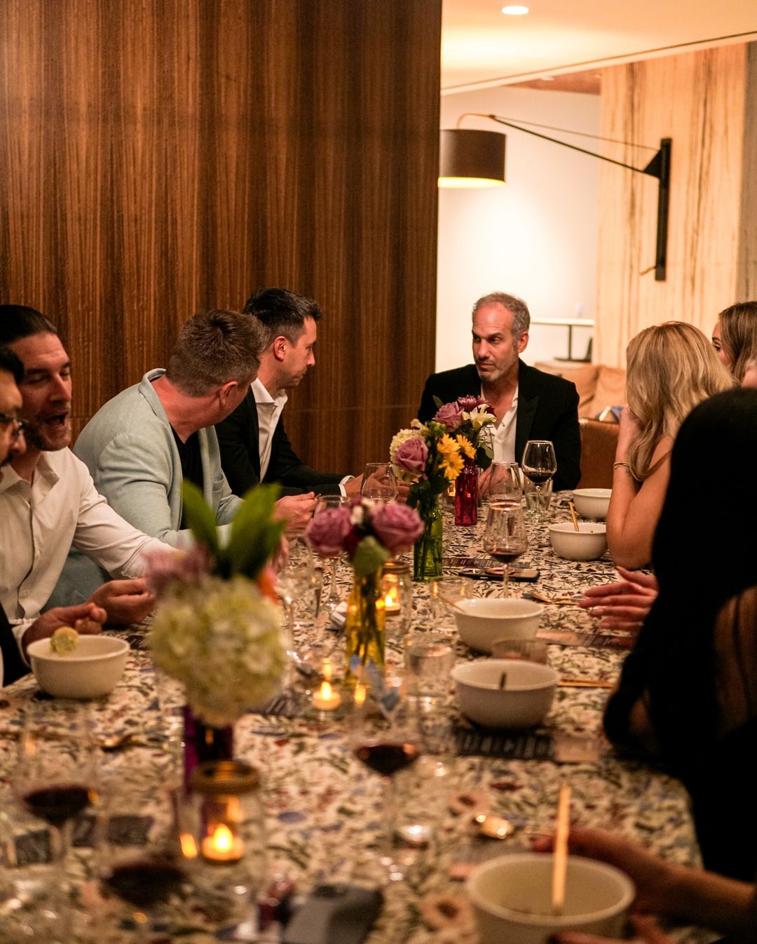 Guests at a long candlelit table with floral linens and city views