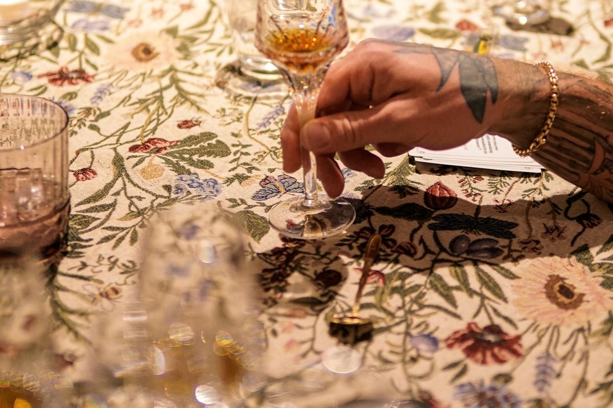 A guest raises a crystal glass of cognac over a floral tablecloth