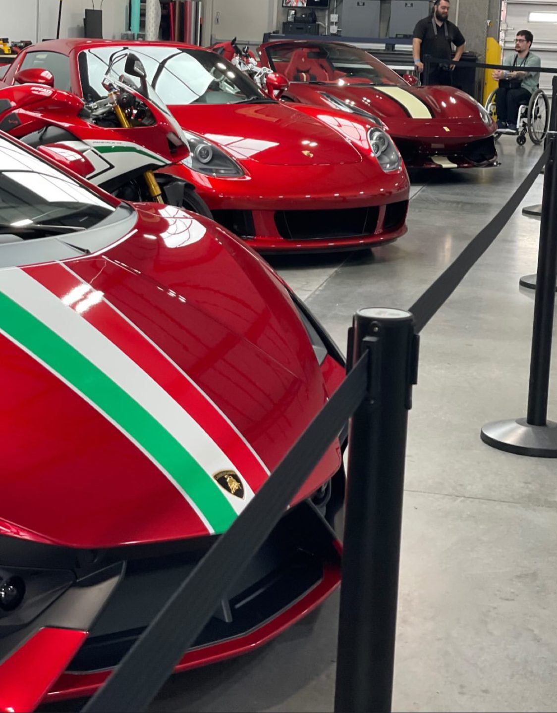 A red Lamborghini with an Italian-flag stripe behind a stanchion rope